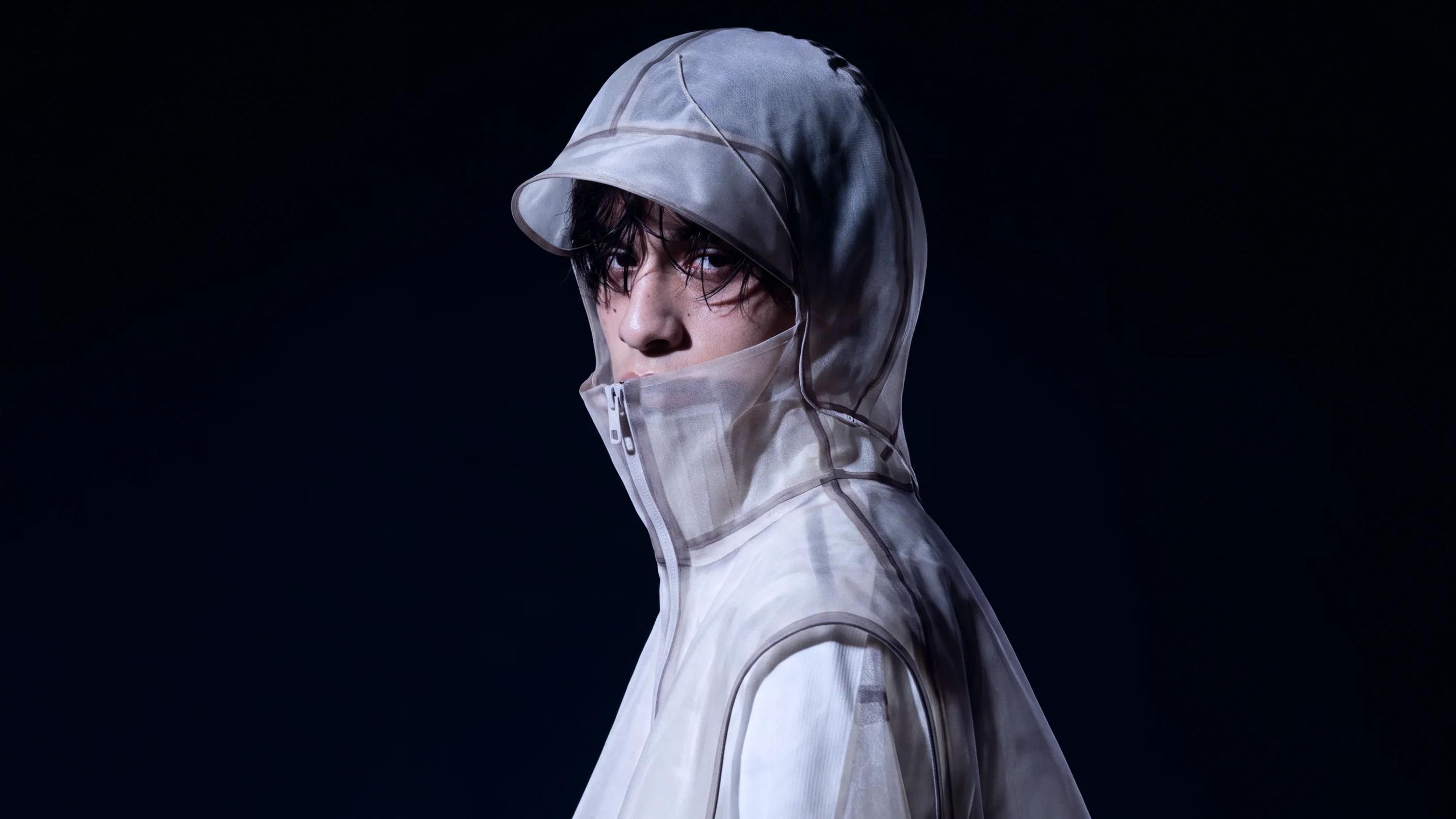 Portrait in a translucent hooded KIPRUN garment against a dark background