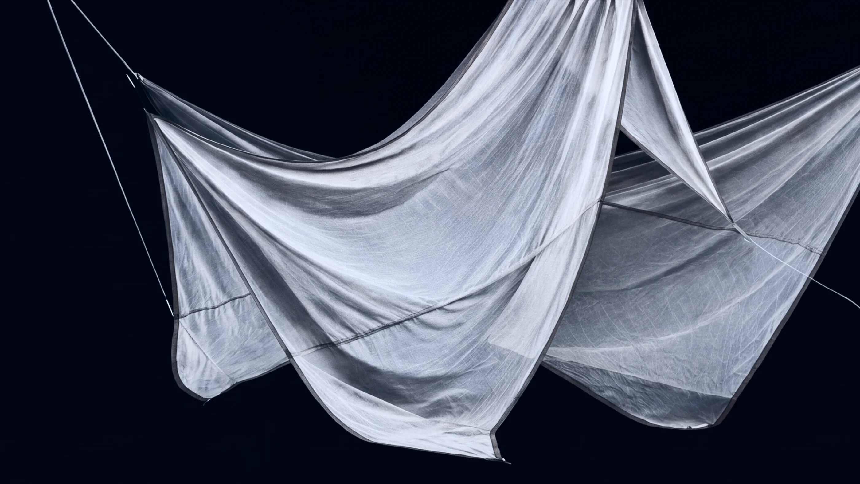 Lightweight translucent fabric suspended in flowing folds against a dark background